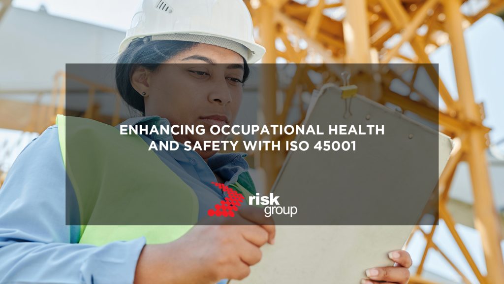 A banner image designed to promote Risk Group's blog post. The background image shows a business executive wearing PPE while reviewing documentation on site. A text overlay reads: "Enhancing Occupational Health & Safety with ISO 45001".